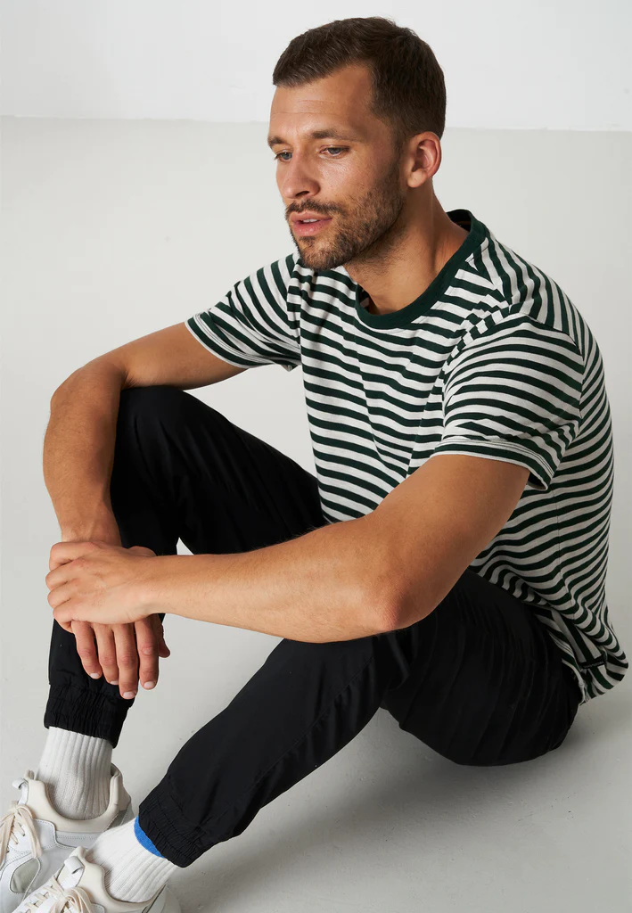 man sitting for a photoshoot wearing stripe t shirt, sneaker and black joggers 