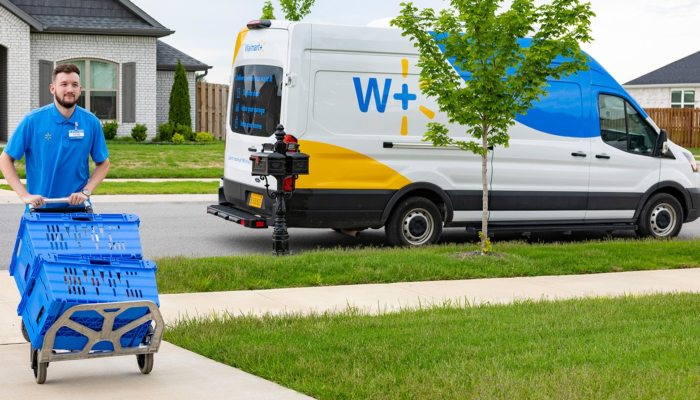 An associate is shown pushing a dolly with two blue bins up a driveway. A Walmart van is parked at the curb