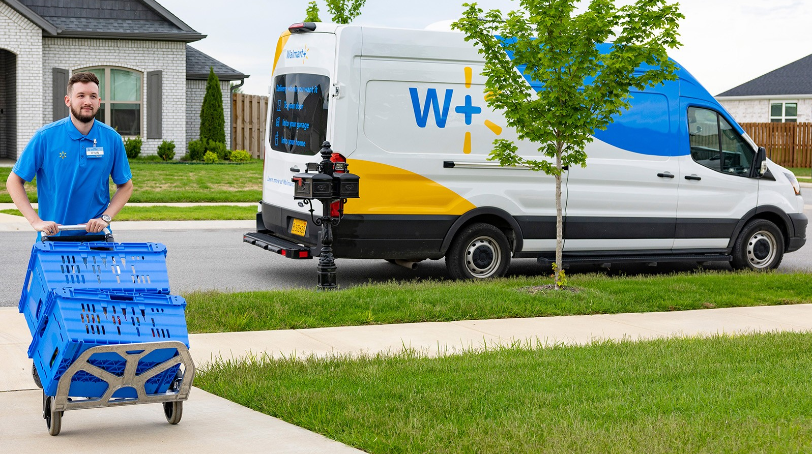 An associate is shown pushing a dolly with two blue bins up a driveway. A Walmart van is parked at the curb