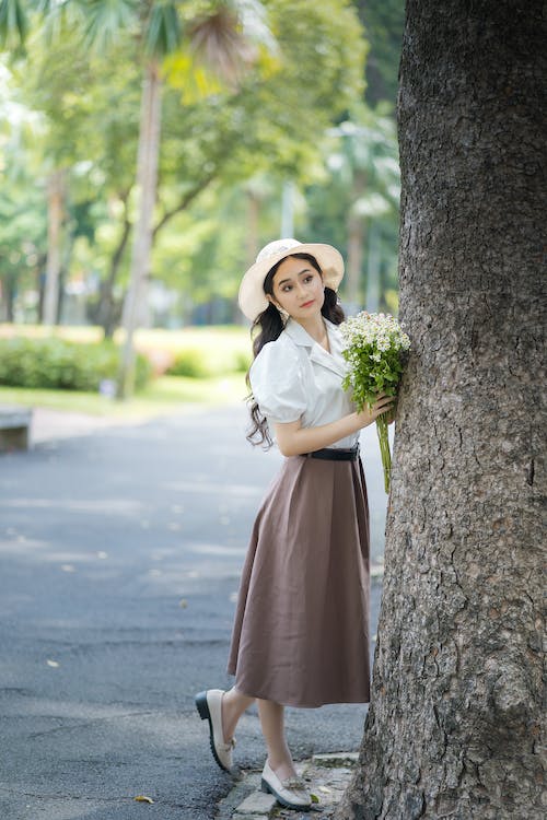 women in white shirt and brown skirt holding flower in hand