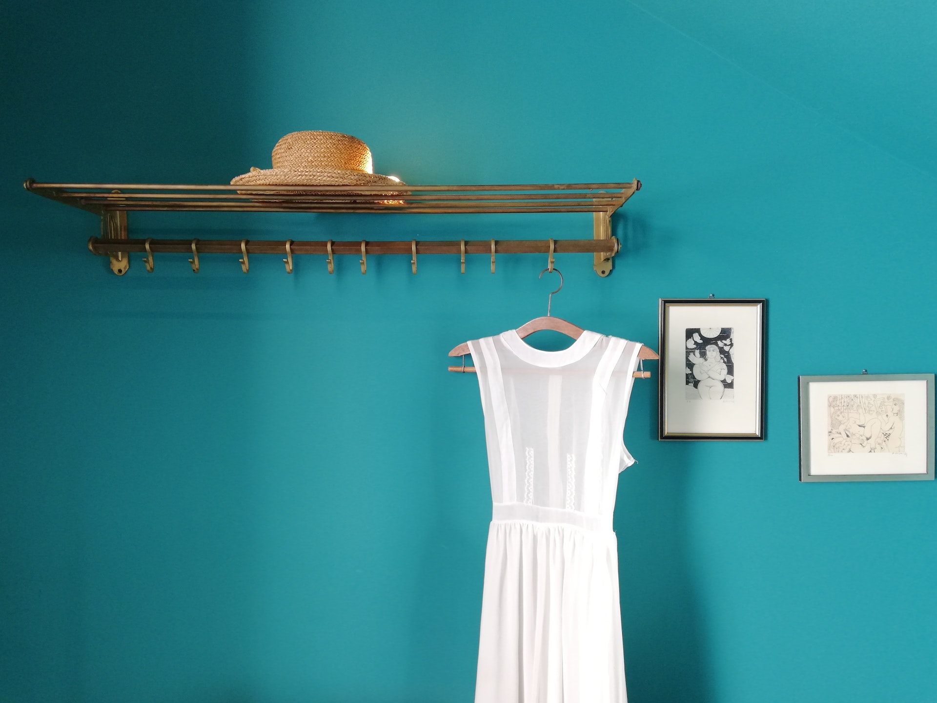 Hanger with straw hat and white dress near blue wall