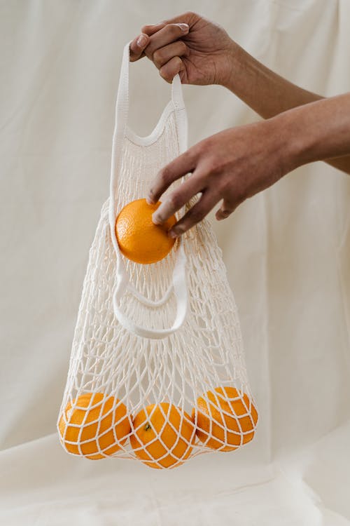 person putting yellow colored fruit in a carrying bag made of fabric