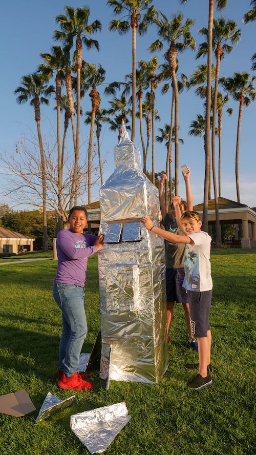 two kid holding aluminum foil made rocket