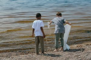 two kid with plastic bag and bottle in hand near sea shore
