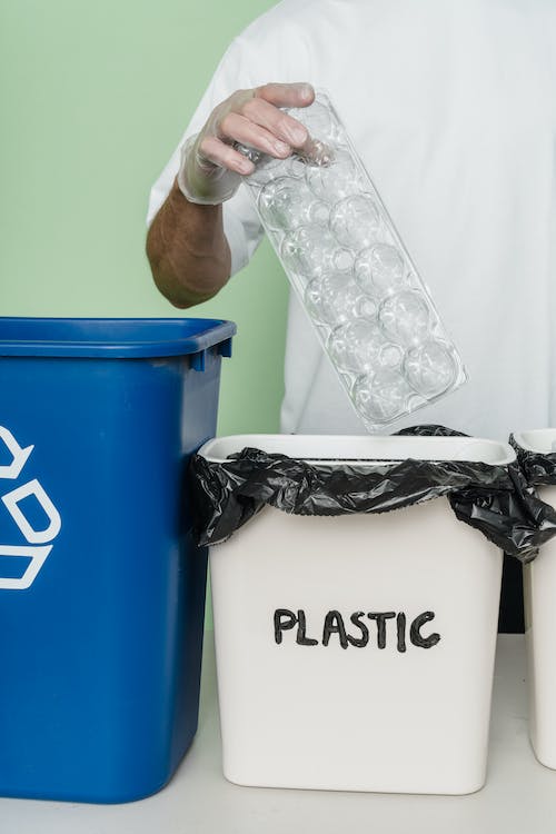 person putting plastic in a white trash bin written plastic on it