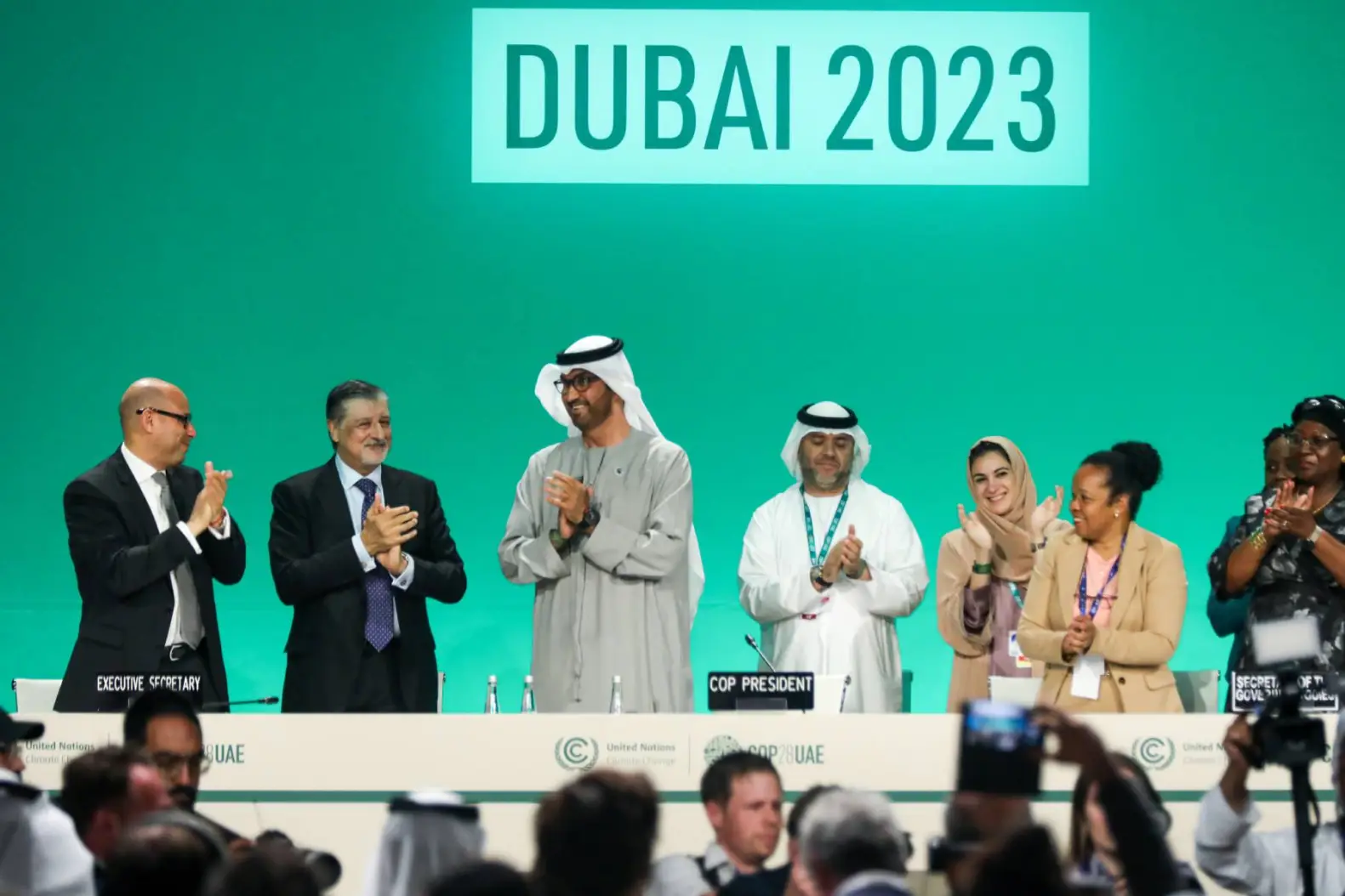 people are clapping in front of a giant screen written Dubai 2023 on it