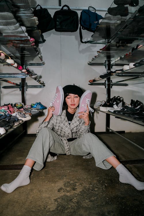 women sitting beside show racks and posing for photo with a pair of pink converse in hand